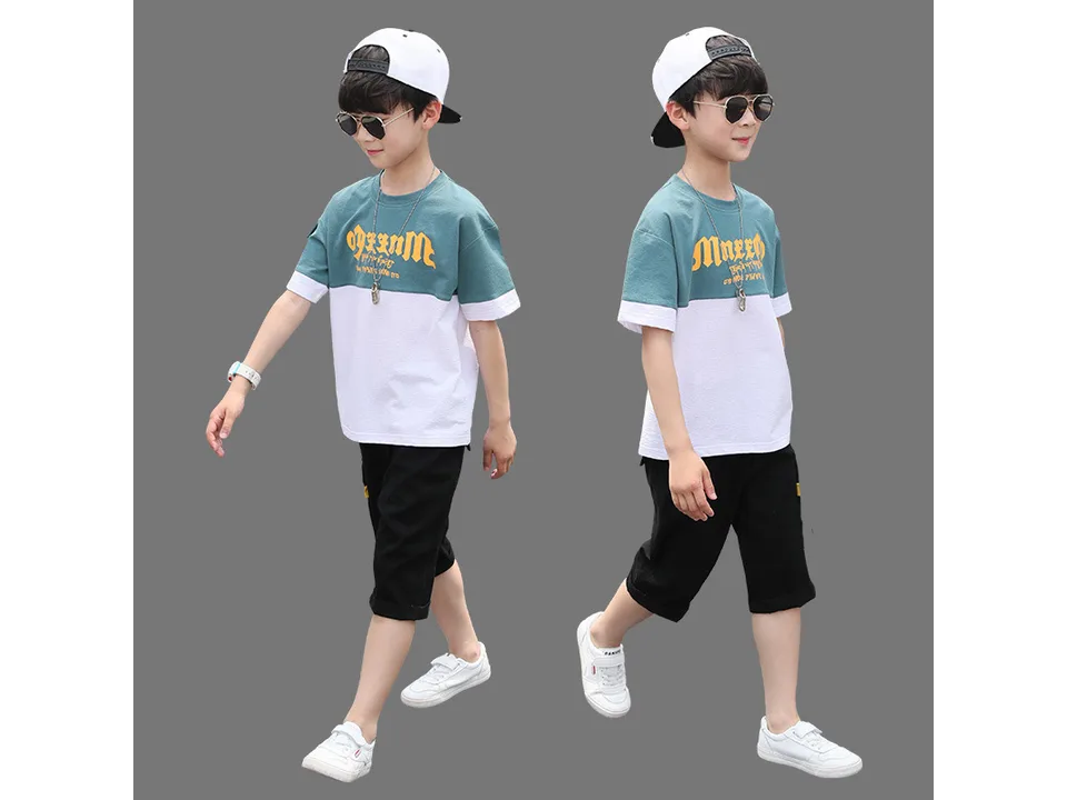 A boy wearing a green and white color-blocked t-shirt and black shorts.