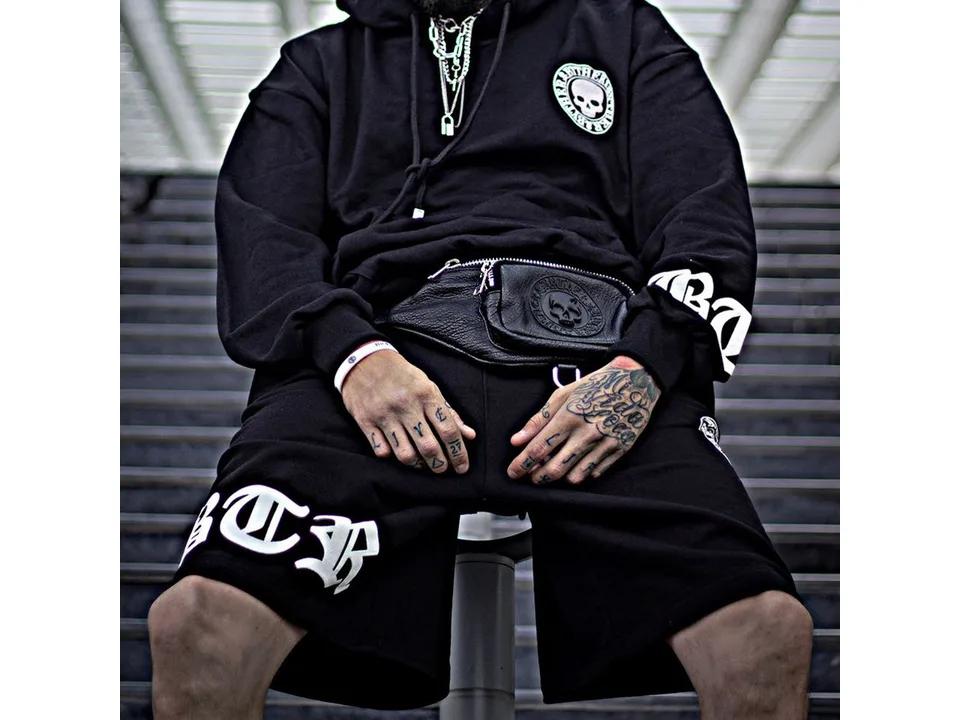 A person wearing black graphic sweatshorts with a skull logo and lettering.
