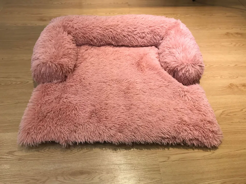 A pink plush pet bed with raised sides on a wooden floor.