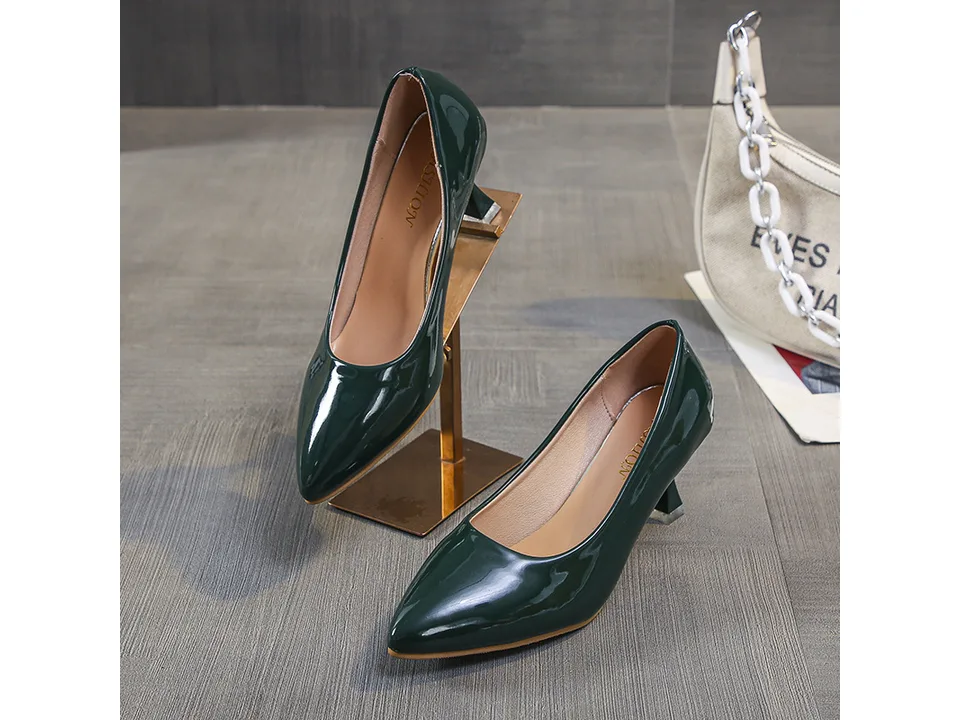 A pair of dark green pointed toe stiletto pumps on a display stand.