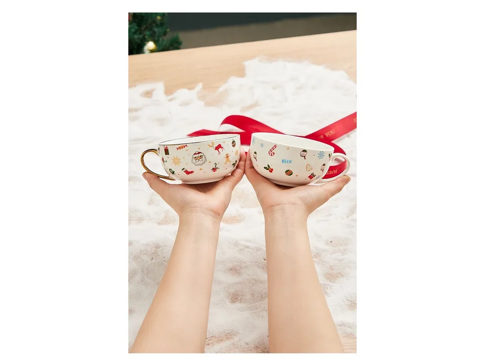 Two hands holding two different Christmas-themed ceramic tea cups.