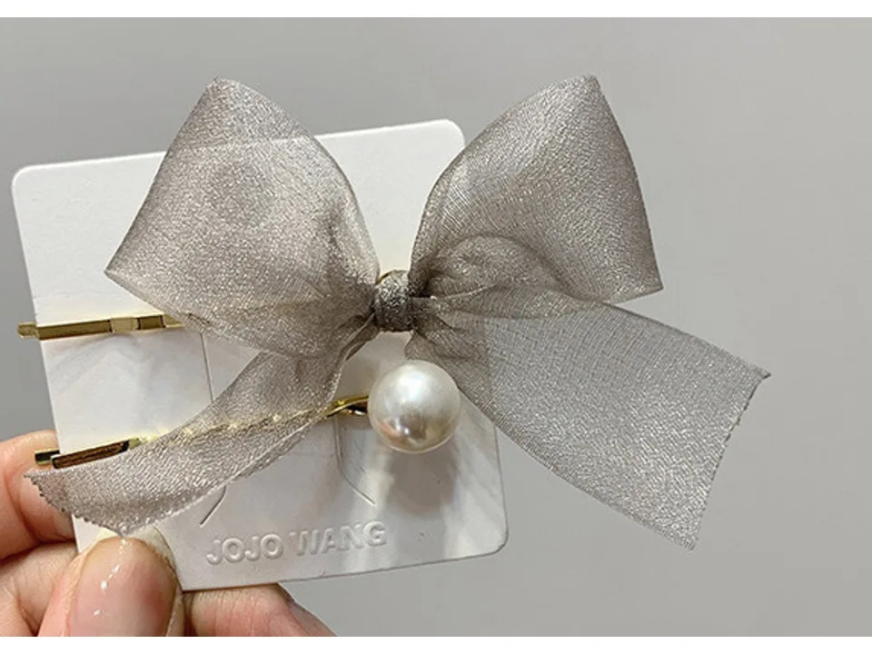 A grey organza bow hair clip with a pearl accent on a display card.