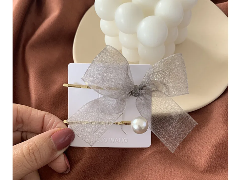 The grey bow and pearl hair clip resting on a surface next to a decorative candle.