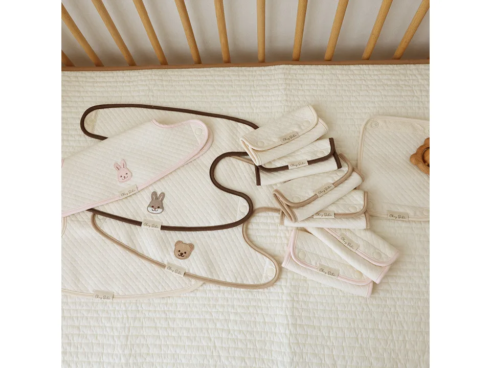 A collection of baby carrier protective covers with various animal embroidery designs laid out on a bed.