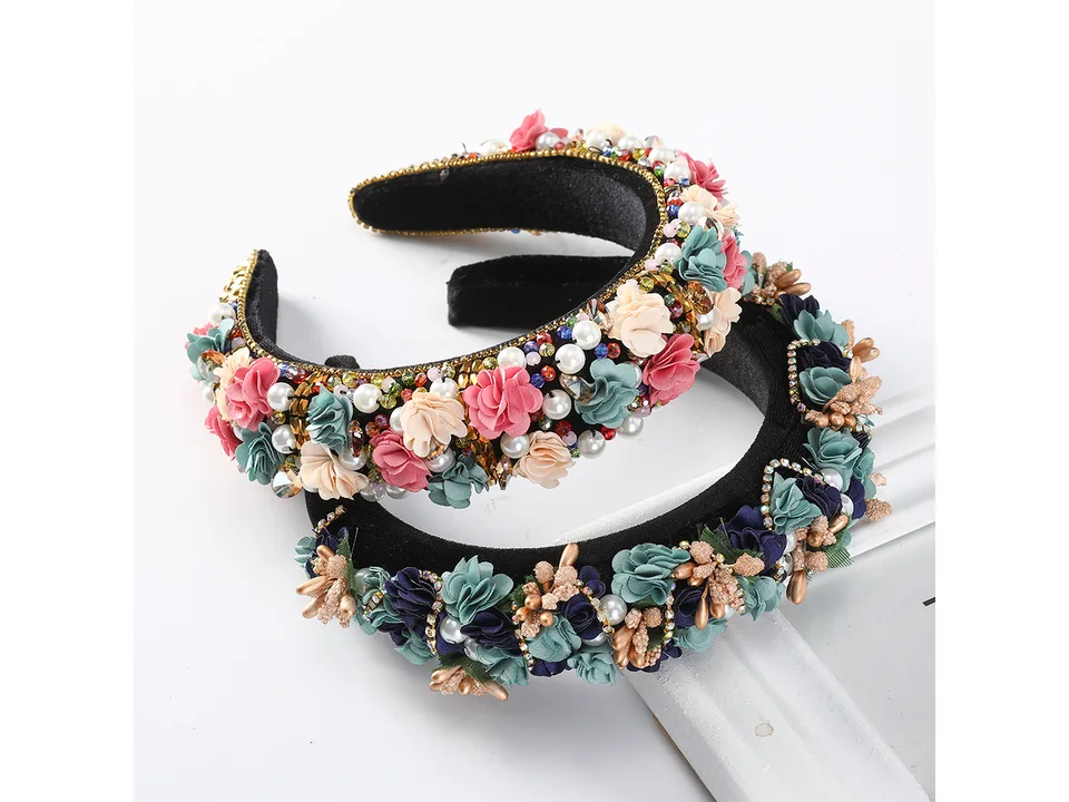 A bridal headband with fabric flowers and pearls held in a hand.