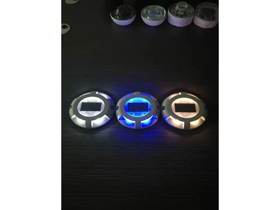 Three solar ground lights glowing in white, blue, and warm yellow light.