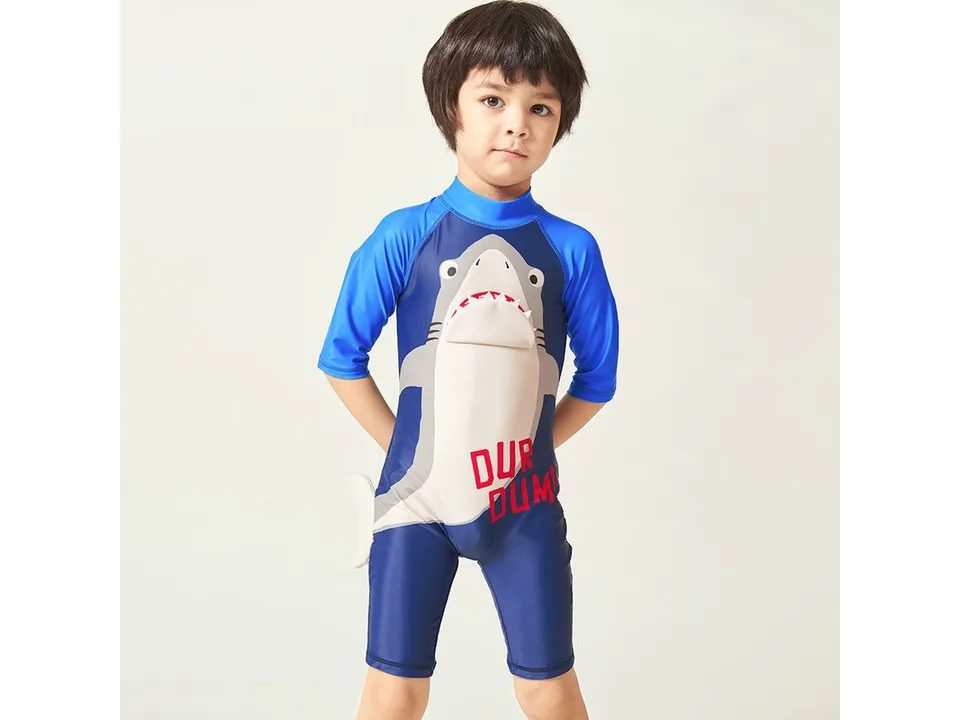 A young boy wearing a blue shark-themed one-piece swimsuit.