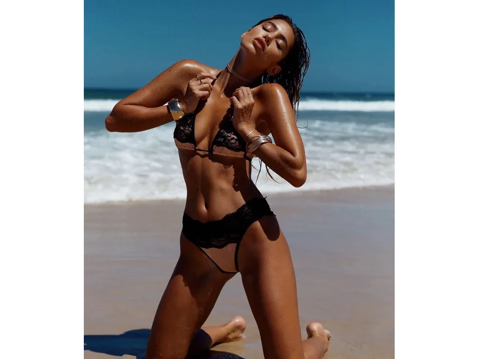 A woman kneeling on the beach wearing a black and beige lace bikini set.