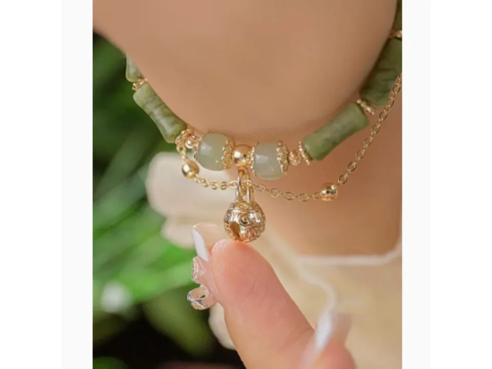 Close-up of the green stone bracelet with a gold bell charm on a wrist.