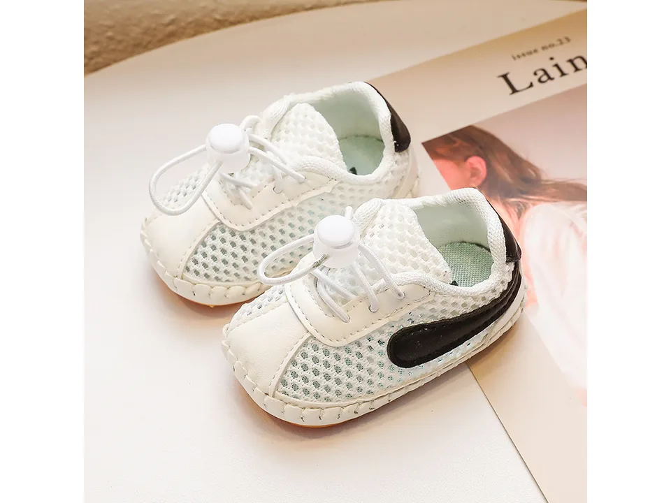 A pair of white mesh baby sneakers with black accents.
