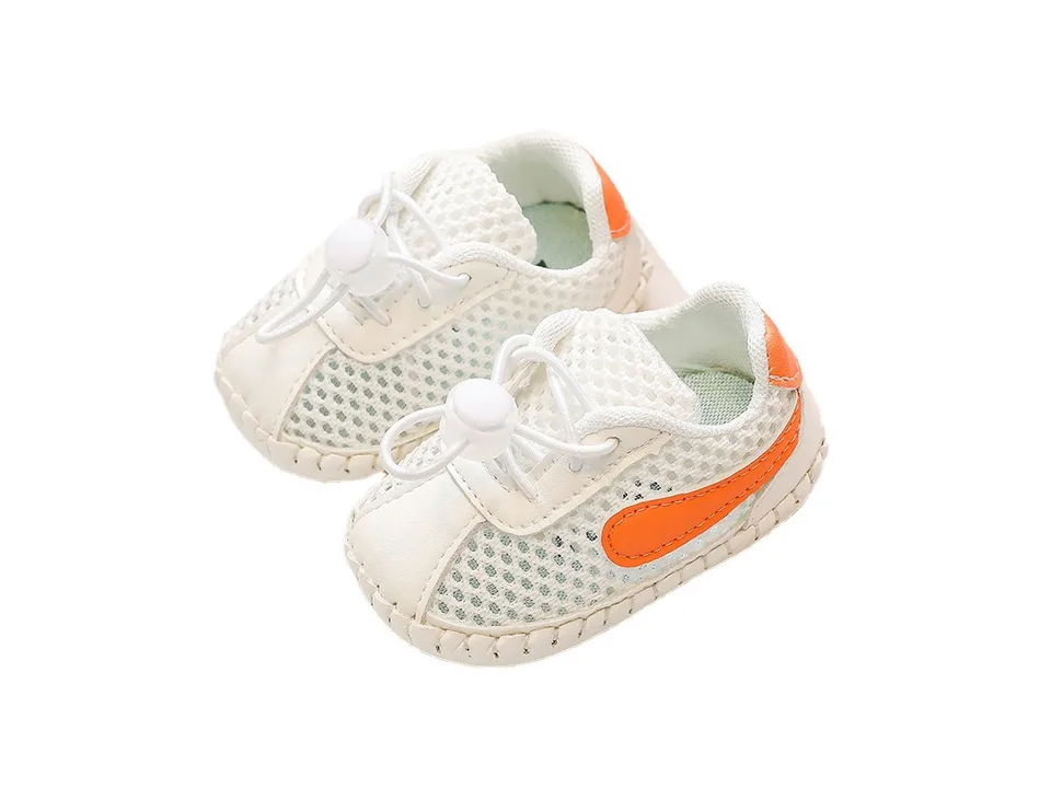 A pair of white mesh baby sneakers with orange accents.