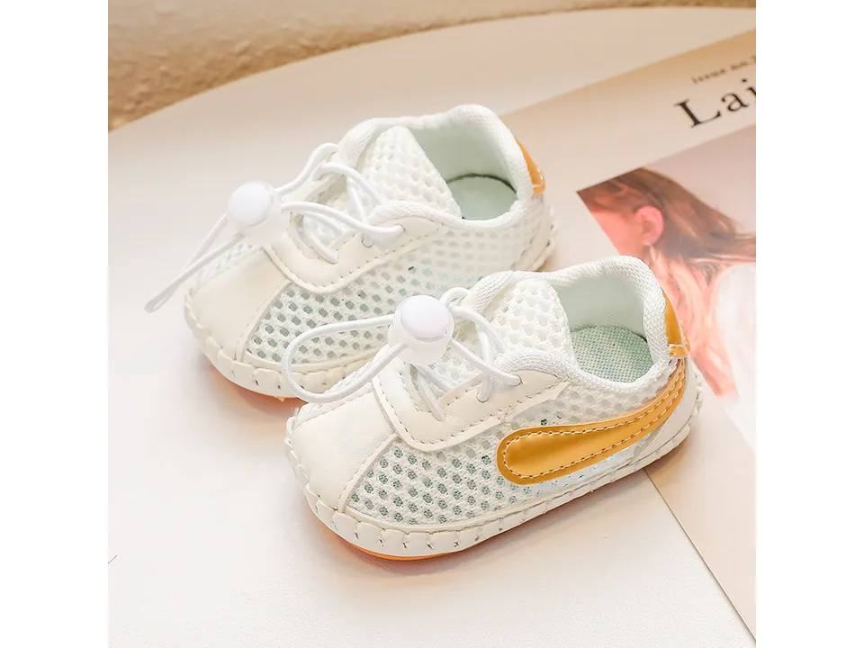 A pair of white mesh baby sneakers with yellow accents.