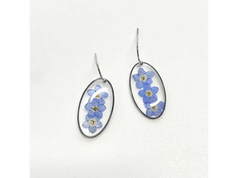 A pair of oval-shaped resin earrings containing blue dried flowers.