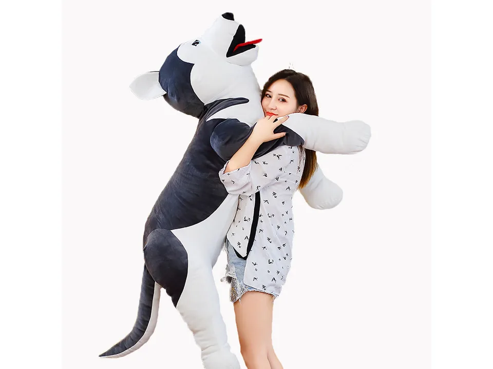 A woman hugging a large husky plush toy.