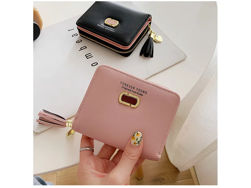 A hand holding a small pink wallet with a tassel charm.