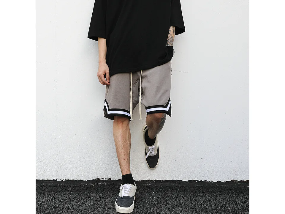 A person wearing grey drawstring sweatshorts with black and white athletic trim.