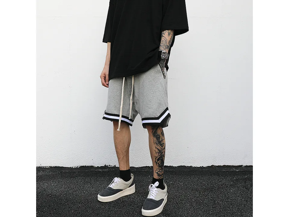 A person wearing light grey drawstring sweatshorts with black and white athletic trim.