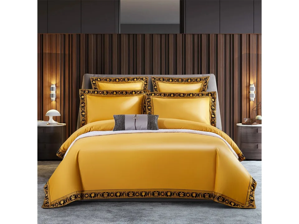 Yellow bedding set with ornate black and gold patterned edges on a bed.