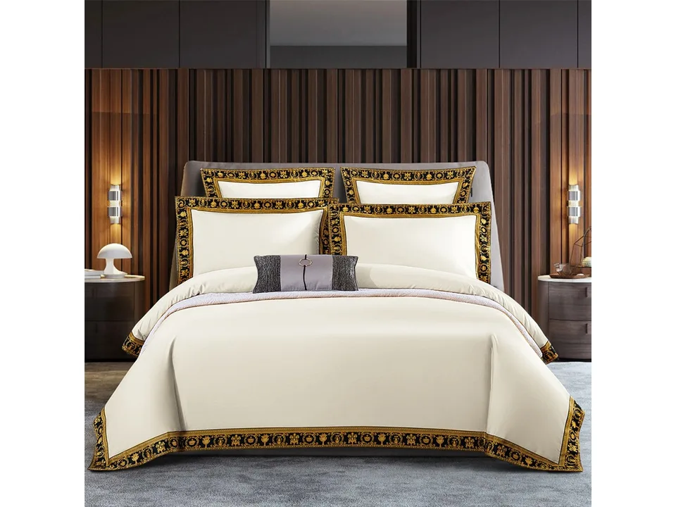 Cream-colored bedding set with ornate black and gold patterned edges on a bed.