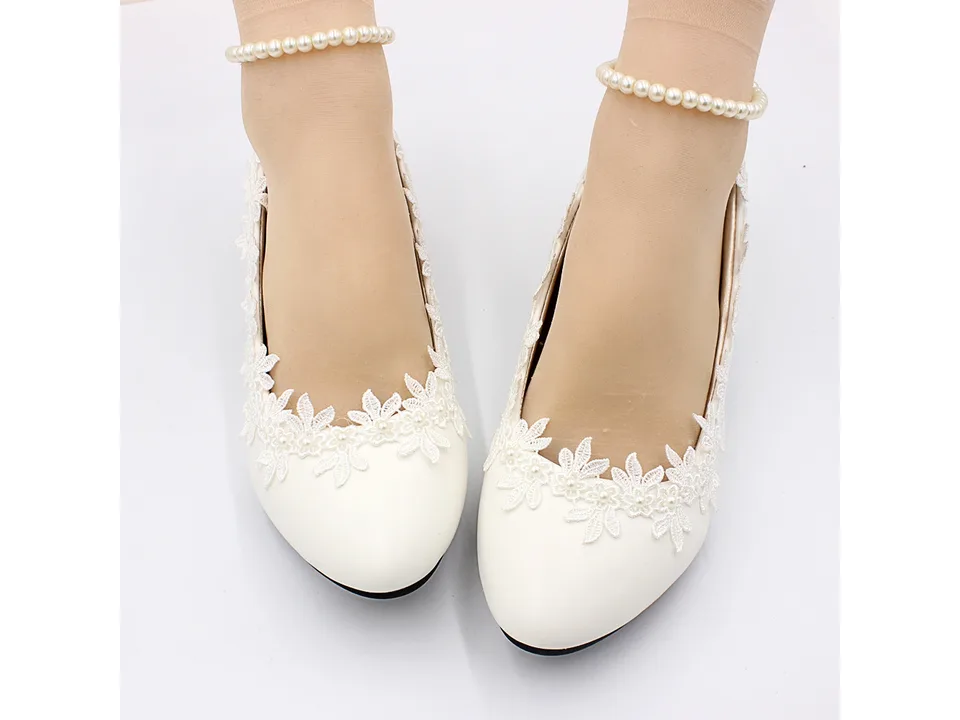 Front view of white lace wedding pumps worn on feet with pearl anklets.
