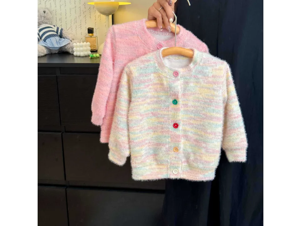 Two knit cardigans with multi-colored buttons hanging on wooden hangers.