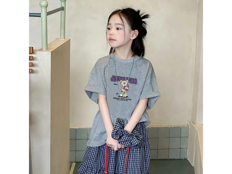 A young girl wearing a grey short-sleeved t-shirt with a bear graphic.