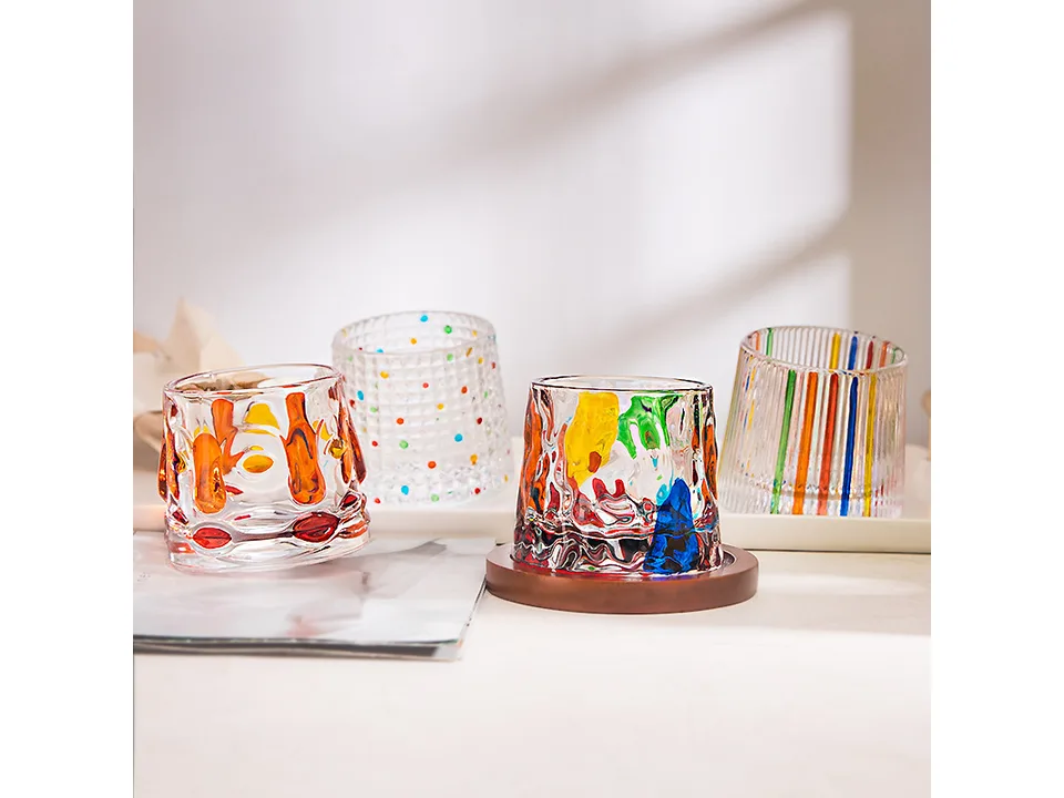 A collection of colorful spinning tumbler glasses with wooden coasters on a table.