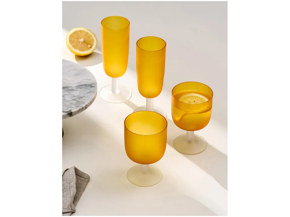 Four orange frosted glass goblets on a white surface with a lemon slice.