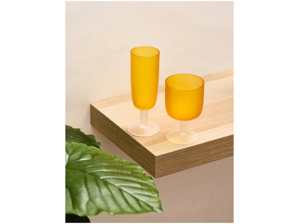 Two orange frosted glass goblets on a wooden shelf next to a green plant.