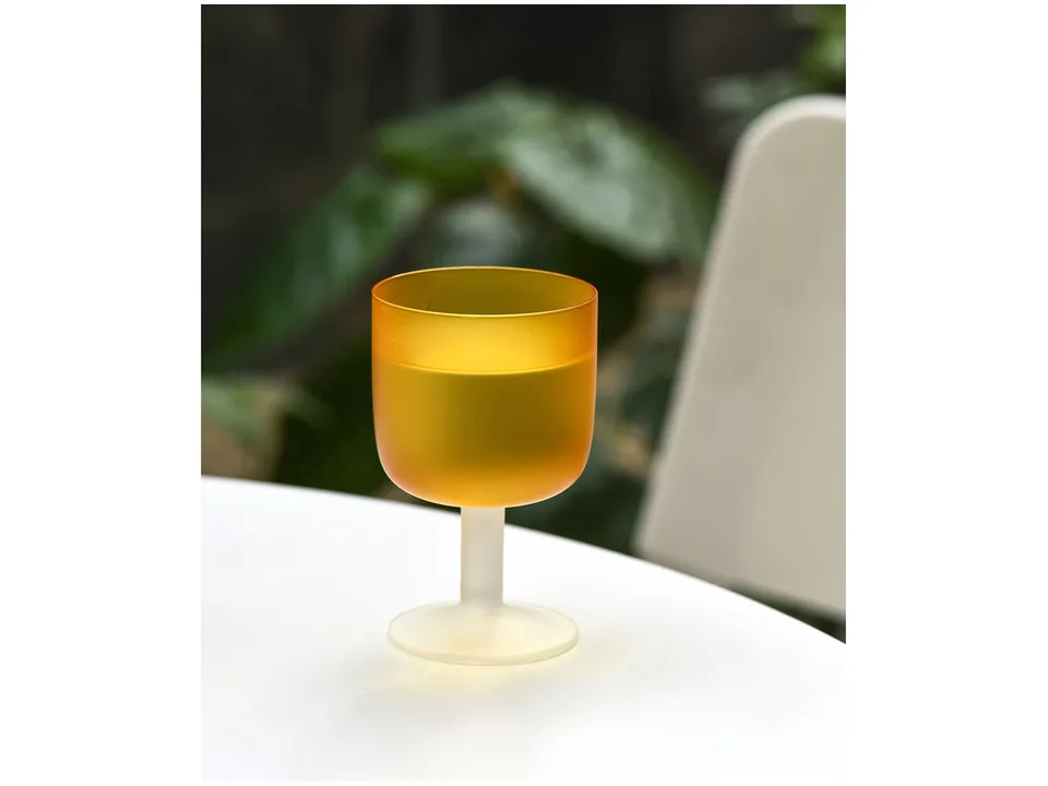 A single orange frosted glass goblet on a white table.