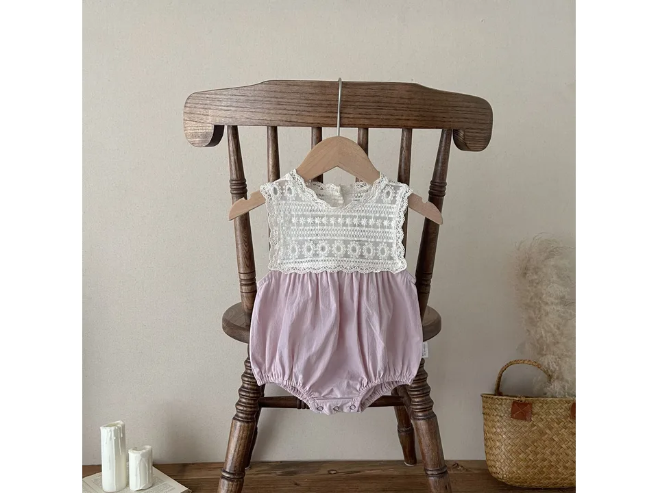 Pink baby romper with lace bodice hanging on a wooden chair