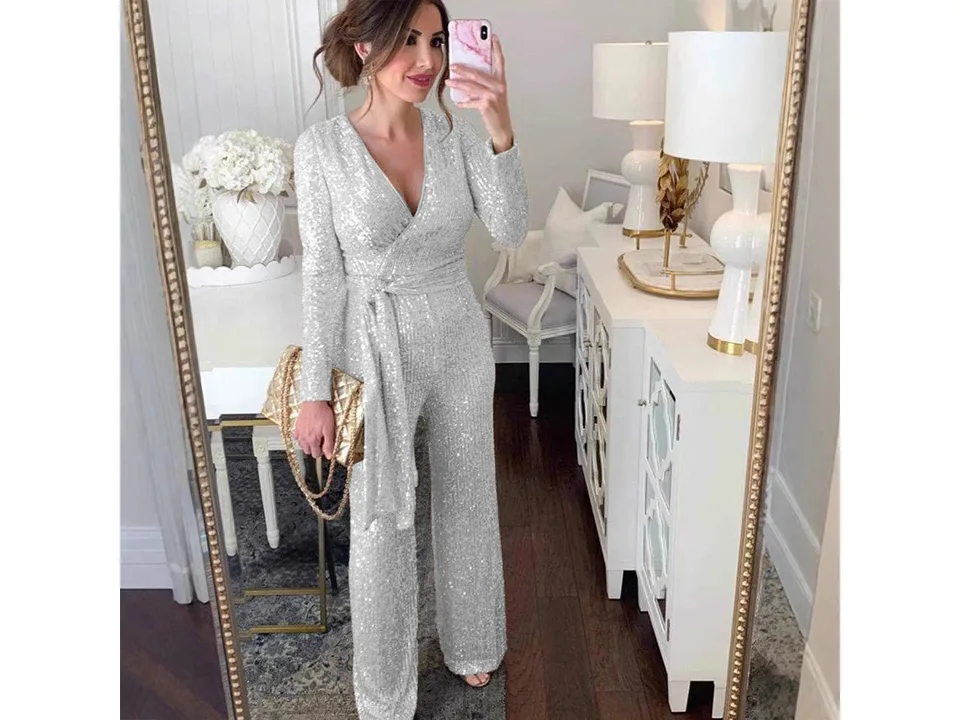 A woman wearing a silver long-sleeve sequin jumpsuit with a waist tie.