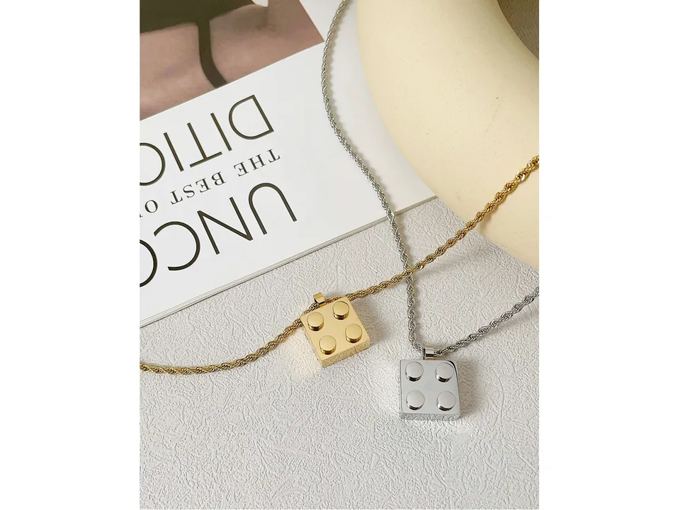 Gold and silver building block pendant necklaces resting on a surface.
