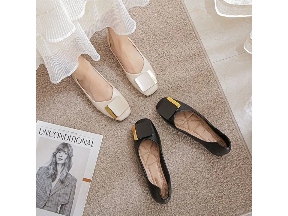 A pair of beige square toe flat loafers being worn, with a pair of black loafers nearby.