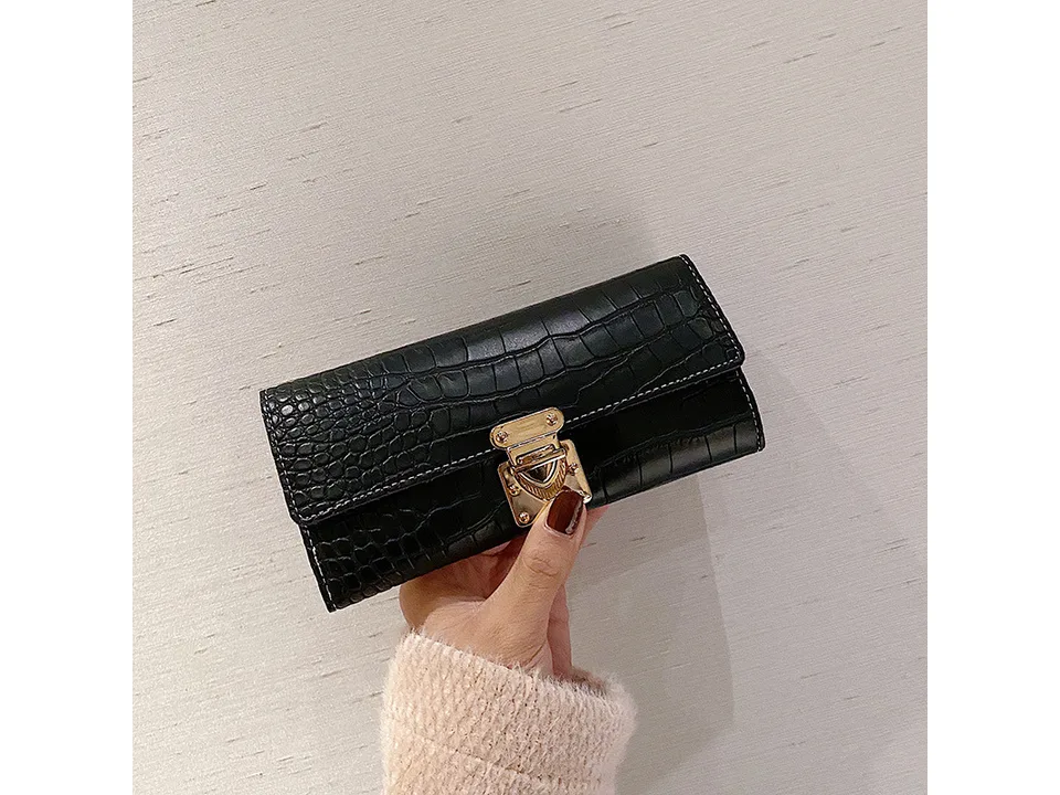 A black crocodile pattern long wallet with a gold lock closure held in a hand.