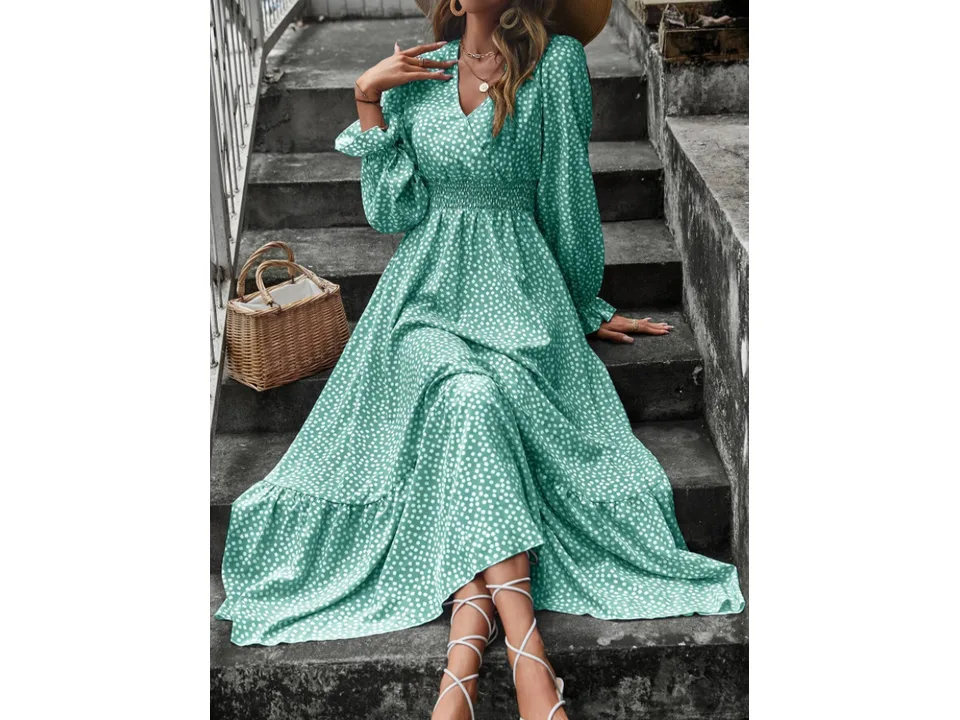 A woman wearing a green floral V-neck maxi dress with long sleeves and a smocked waist, sitting on stone steps.