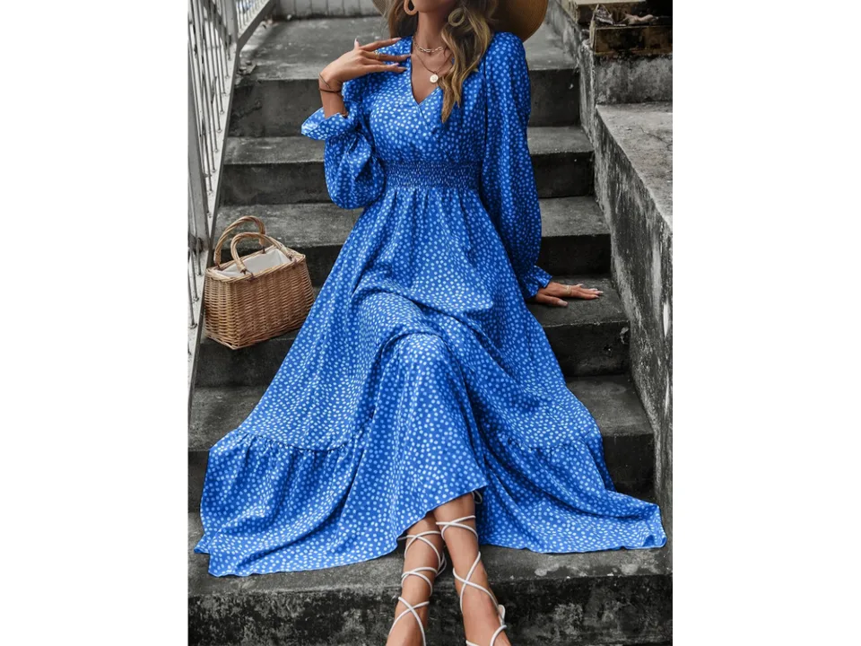 A woman wearing a blue floral V-neck maxi dress with long sleeves and a smocked waist, sitting on stone steps.