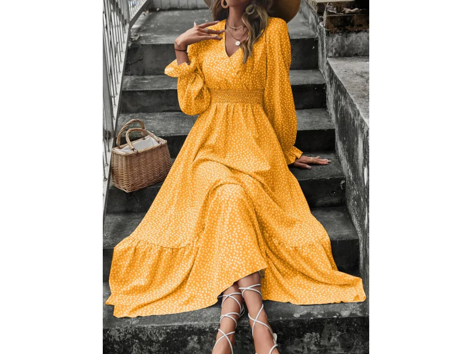 A woman wearing a yellow floral V-neck maxi dress with long sleeves and a smocked waist, sitting on stone steps.