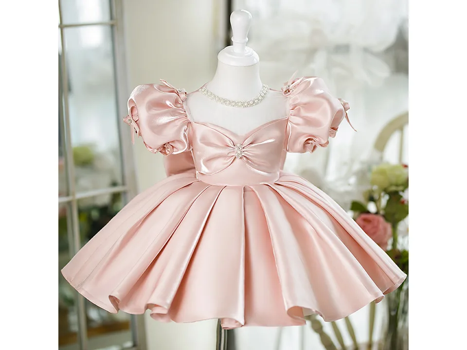 A pink princess ball gown dress on a mannequin, featuring puff sleeves and a bow detail.