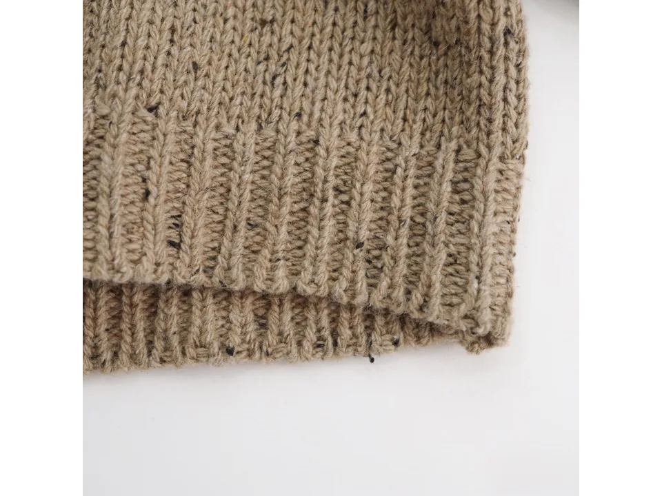 Close-up of the ribbed hem on the beige knitted cardigan.