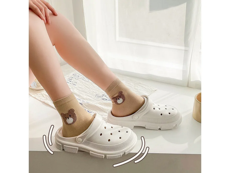 A person wearing white EVA clogs with brown bear socks.