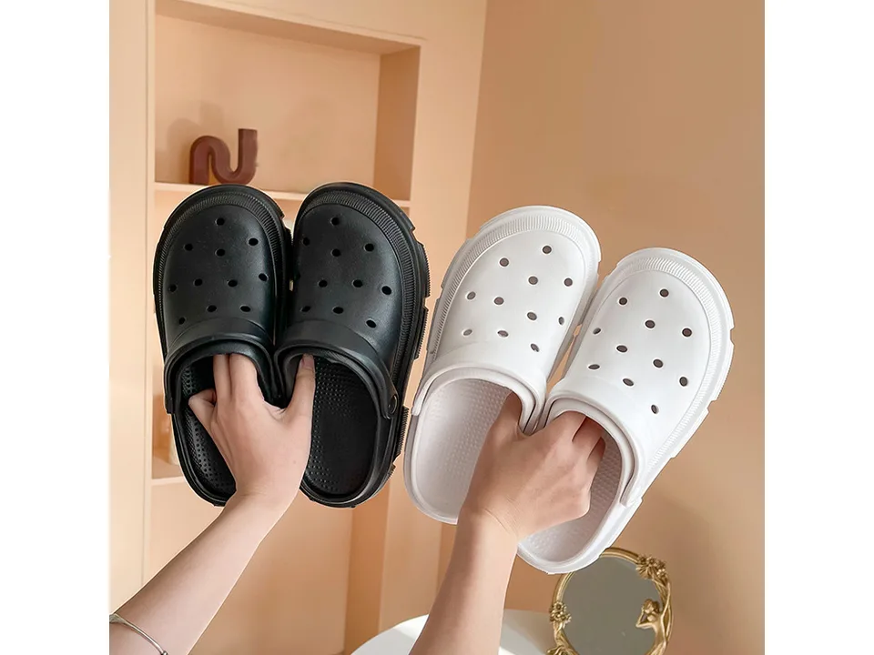 A pair of black and a pair of white EVA garden clogs held up by hands.