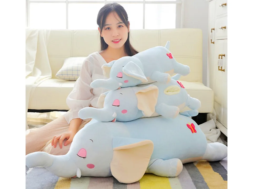 A woman sitting with a stack of three blue elephant plush toys of different sizes.