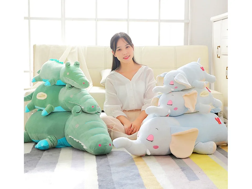 A woman sitting on the floor with several elephant and crocodile plush toys.