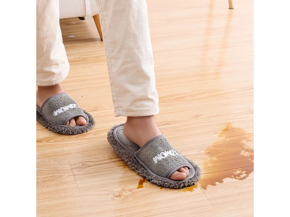 A person wearing grey mop slippers cleaning a spill on a wooden floor.
