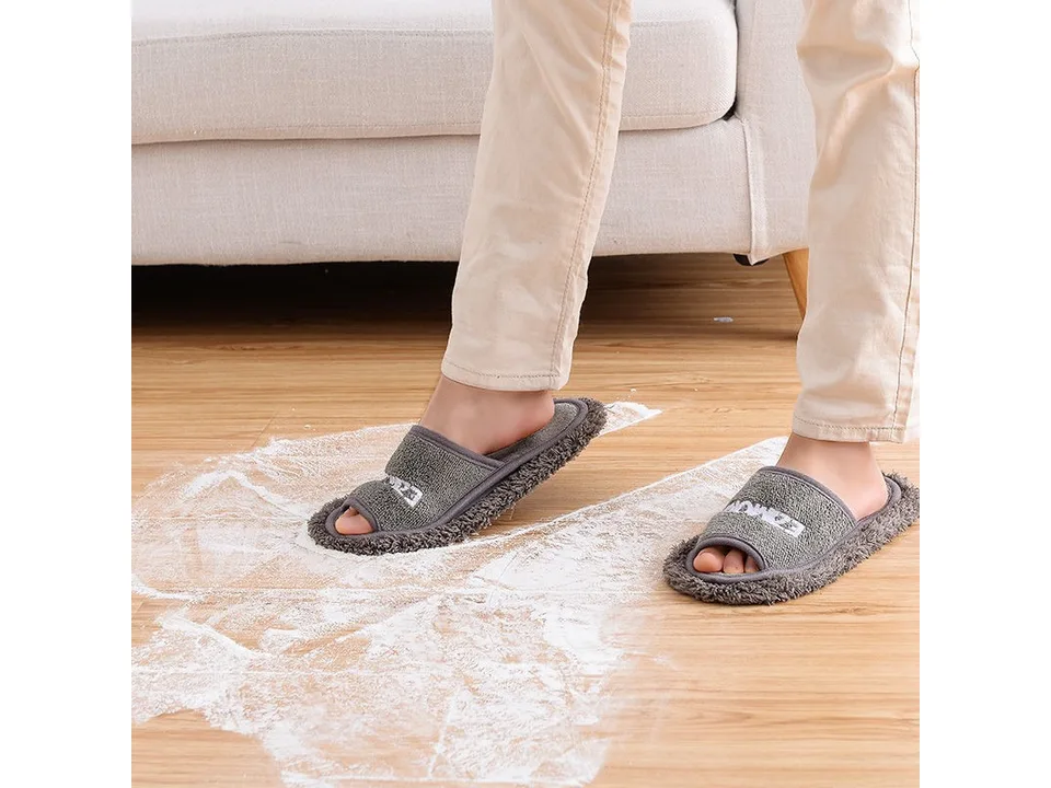 A person wearing grey mop slippers cleaning a dusty floor.