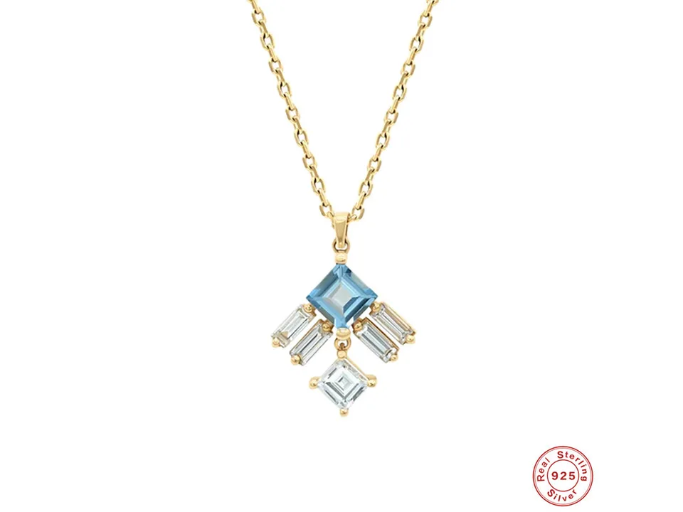 Close-up of the gold pendant necklace featuring a blue square stone and baguette-cut clear stones.