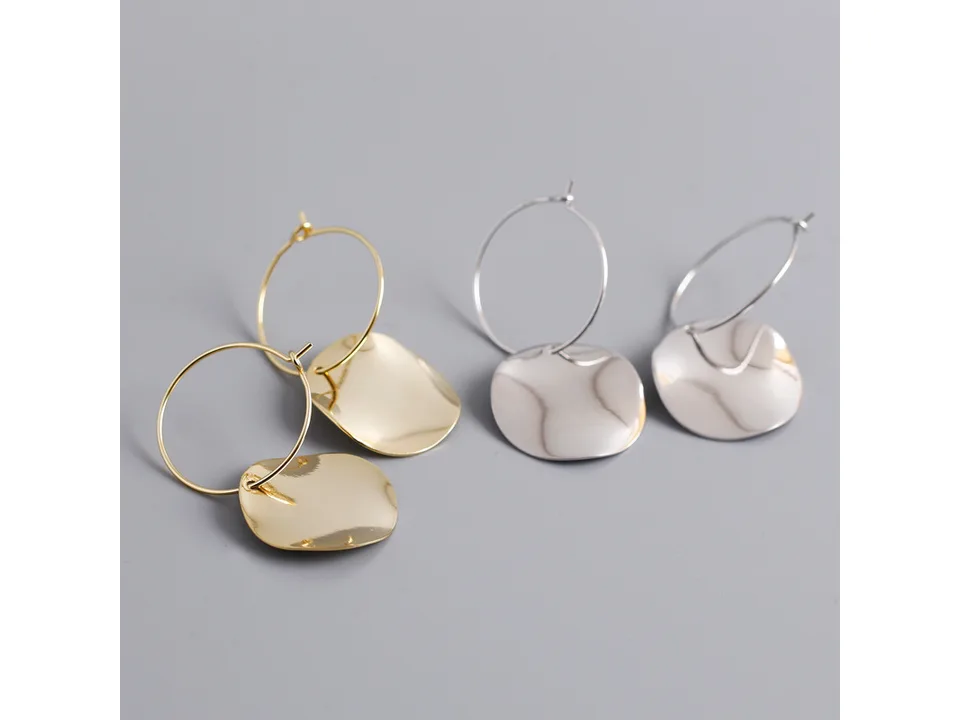 A pair of gold and a pair of silver hoop earrings with wavy disc pendants.