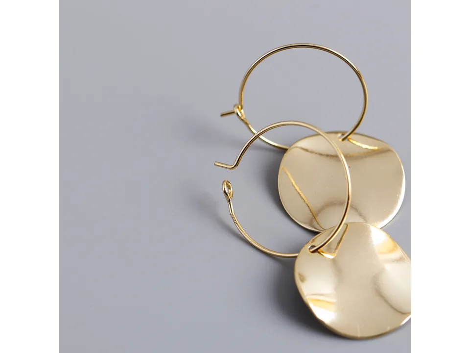 Close-up of gold hoop earrings showing the clasp and the wavy disc detail.