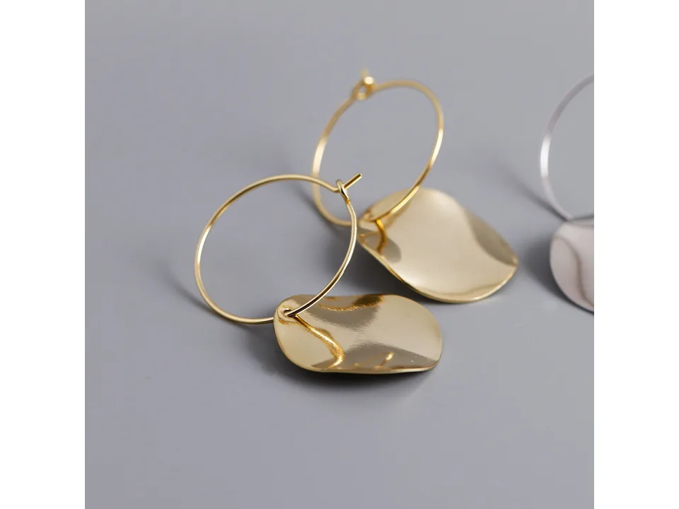 A pair of gold hoop earrings with irregular, wavy disc pendants.